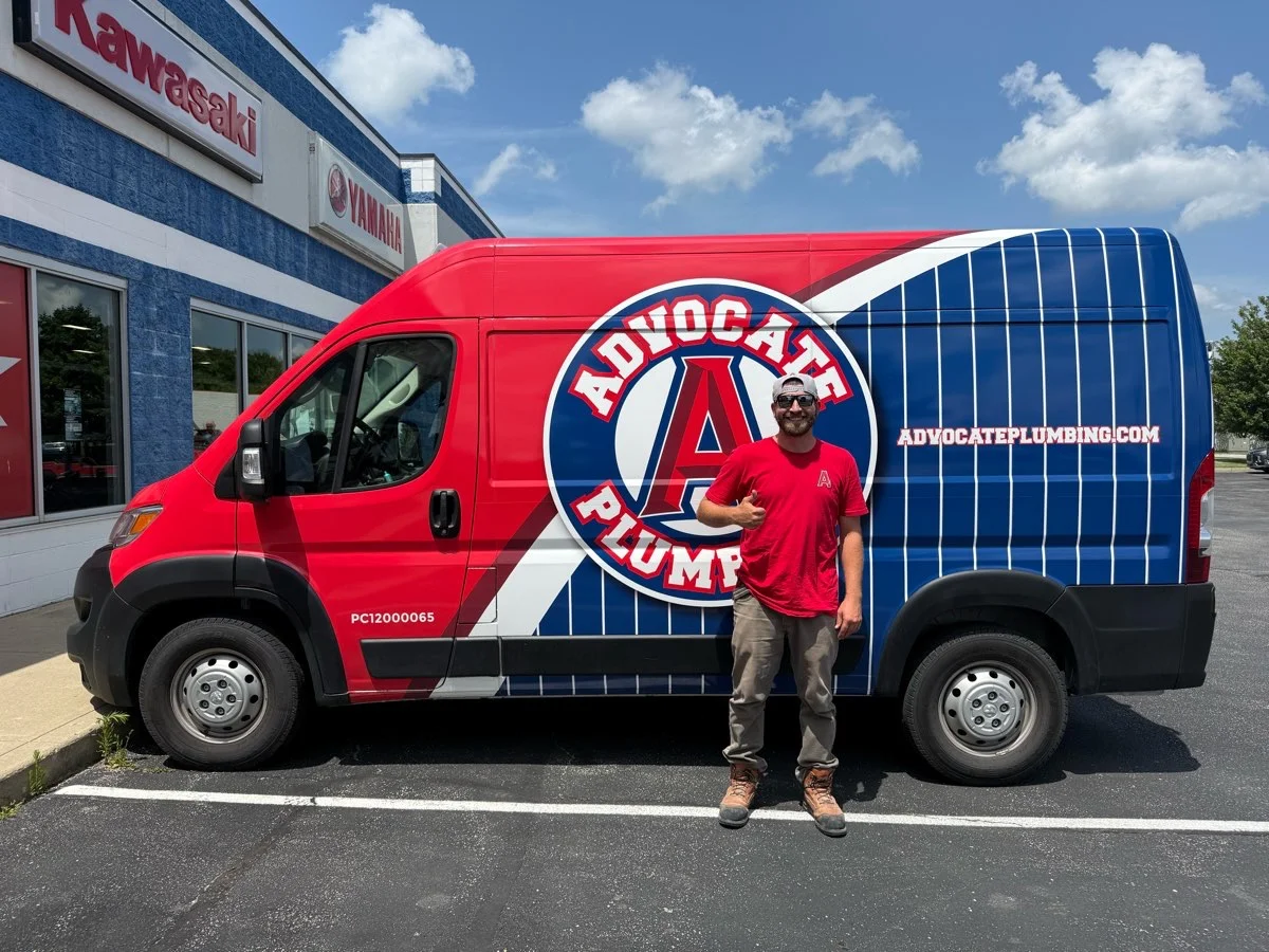 An Advocate Plumbing technician giving a thumbs-up beside the company's red and blue service van